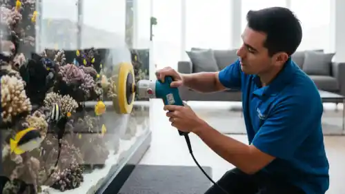 A technician using a buffer to carefully polish a scratch on a large, custom-built acrylic aquarium.